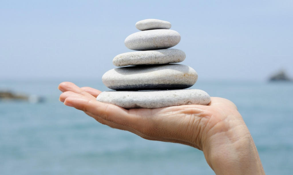 A hand holding a balanced stack of stones, symbolizing energy harmonization and vitality through kinesiology.